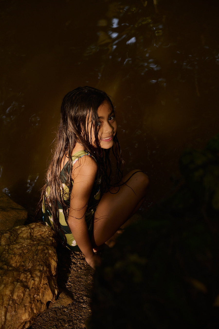 Niña sentada en una roca en la selva al atardecer